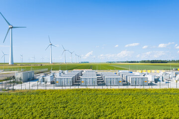 Aerial view of battery energy storage system facility next to wind turbines. Industrial lithium battery system for renewable power plant and grid management.