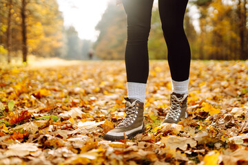 Person in boots walks along forest path surrounded by bright fallen leaves at sunset. Close-up shot shows woman in hiking boots enjoying walk through autumn forest. Hiking and seasonal themes.